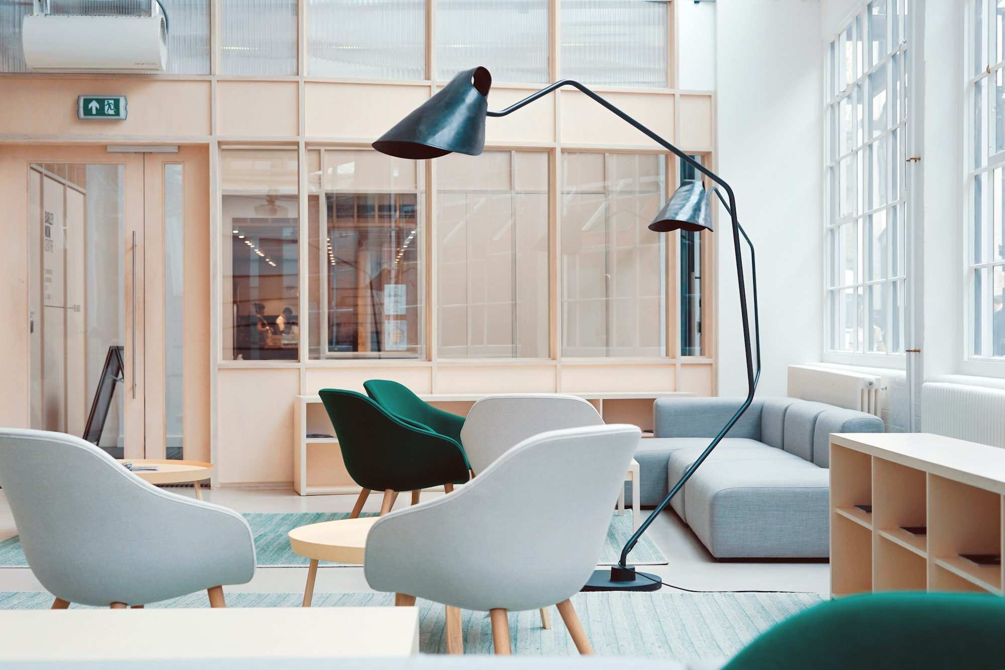 Ljust kontor med stora fönster, fåtöljer och golvlampa.